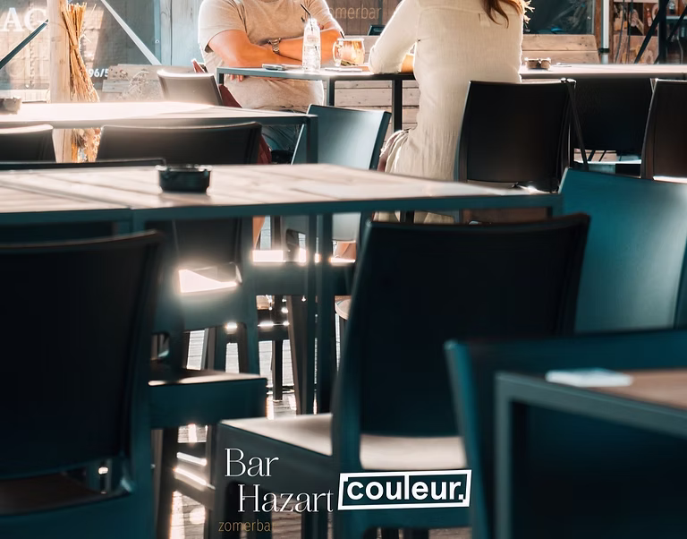 Hoge tafels en zwarte stoelen op het terras van Bar Hazart